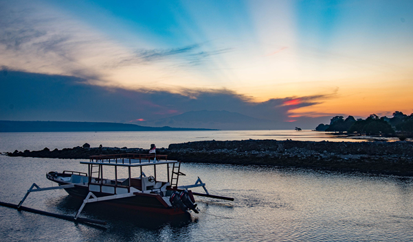 An outrigger boat moored by a stone breakwater at sunset